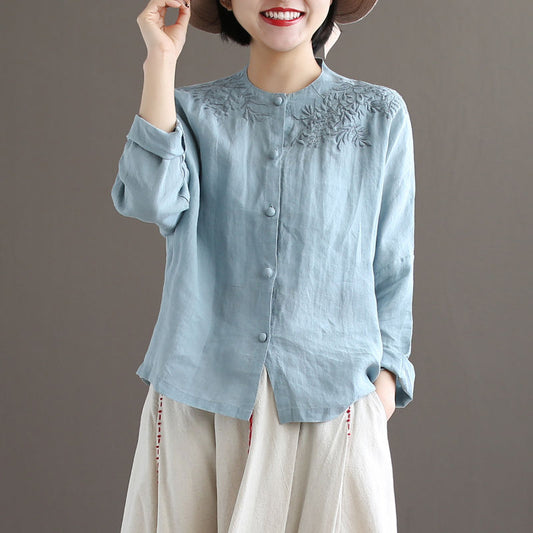 Woman wearing light blue linen embroidered long sleeve blouse with stand collar and button front.