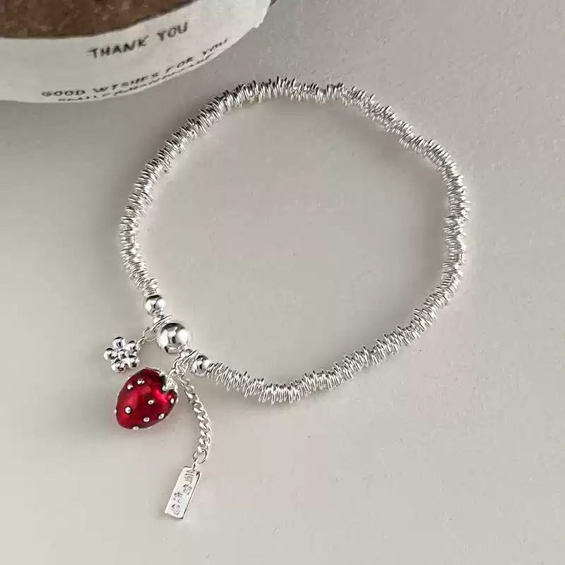 Silver bracelet with a red charm on a light gray background