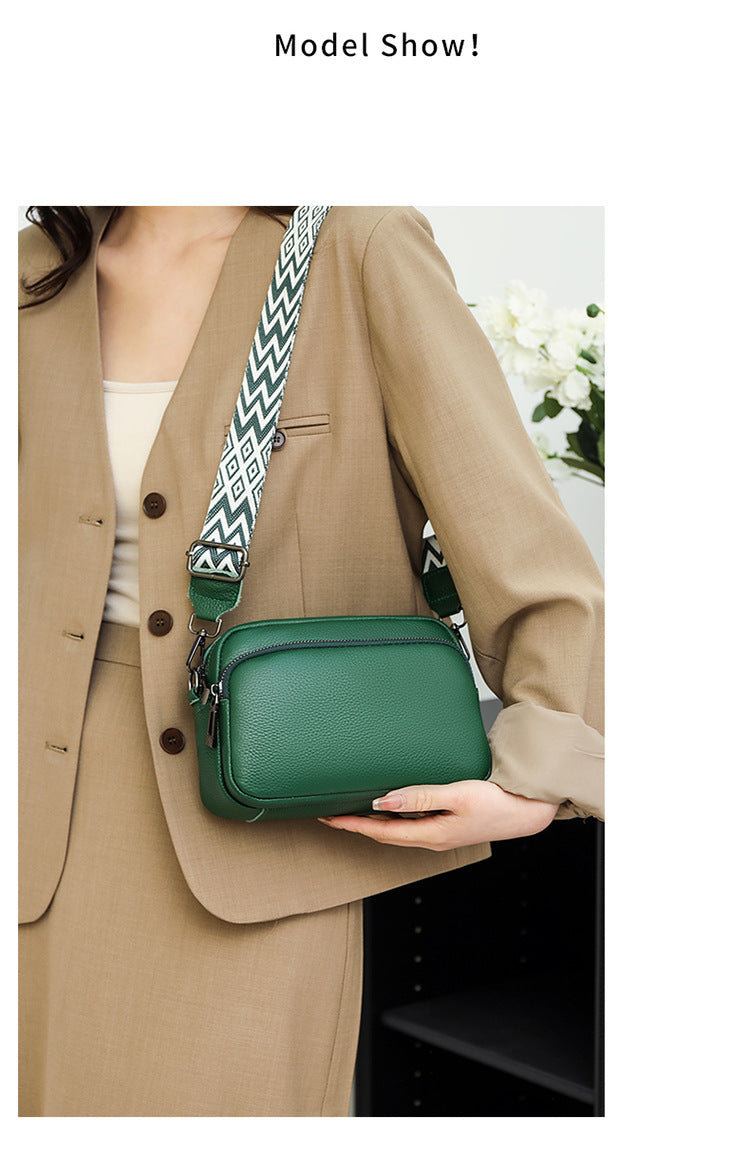 Person holding a green handbag with a patterned strap, wearing a beige suit.
