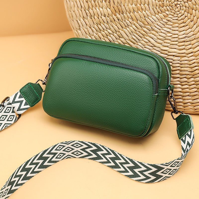 Green handbag with a patterned strap on a beige surface