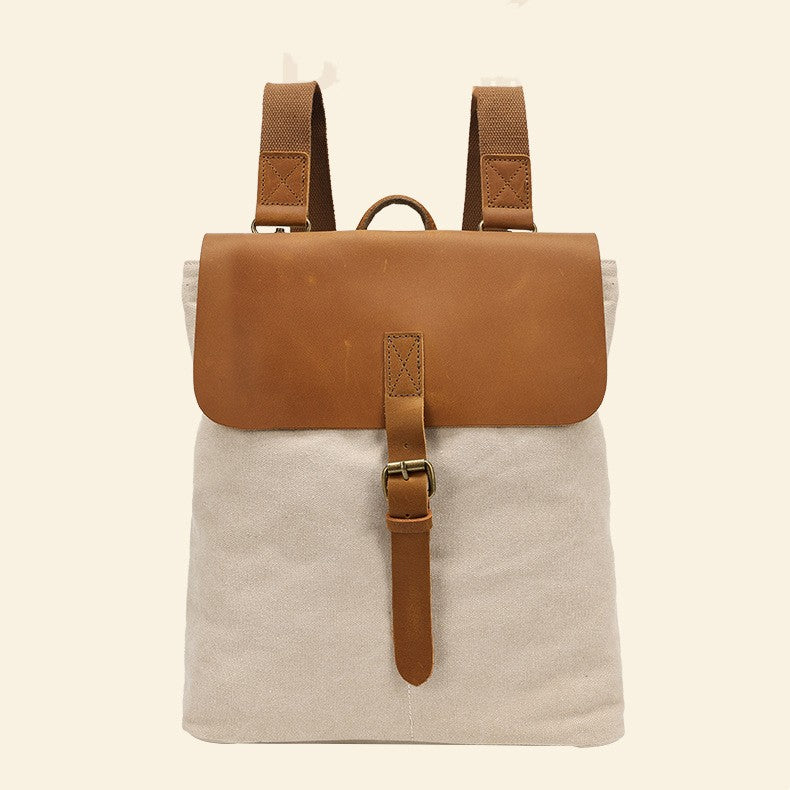 Front view of the white canvas backpack with brown leather flap, buckle closure and adjustable straps