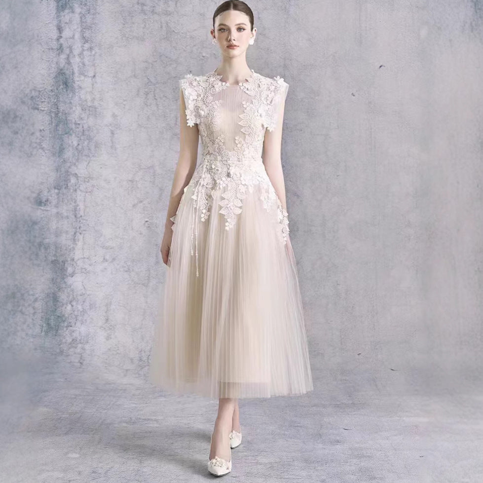 A woman models a sleeveless champagne tulle dress with intricate 3D floral lace appliques on the bodice and waist, set against a textured gray studio backdrop.