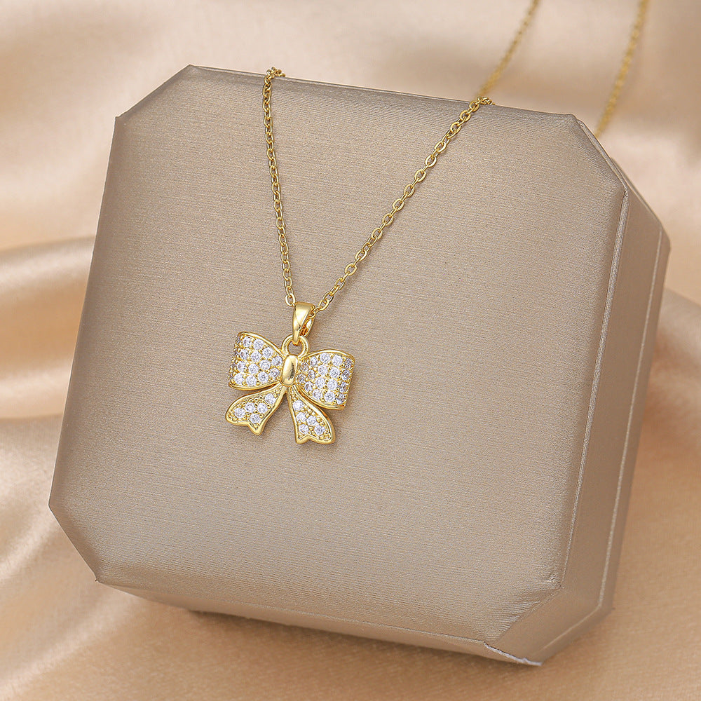 Gold bow zircon pendant necklace on satin display with titanium steel chain