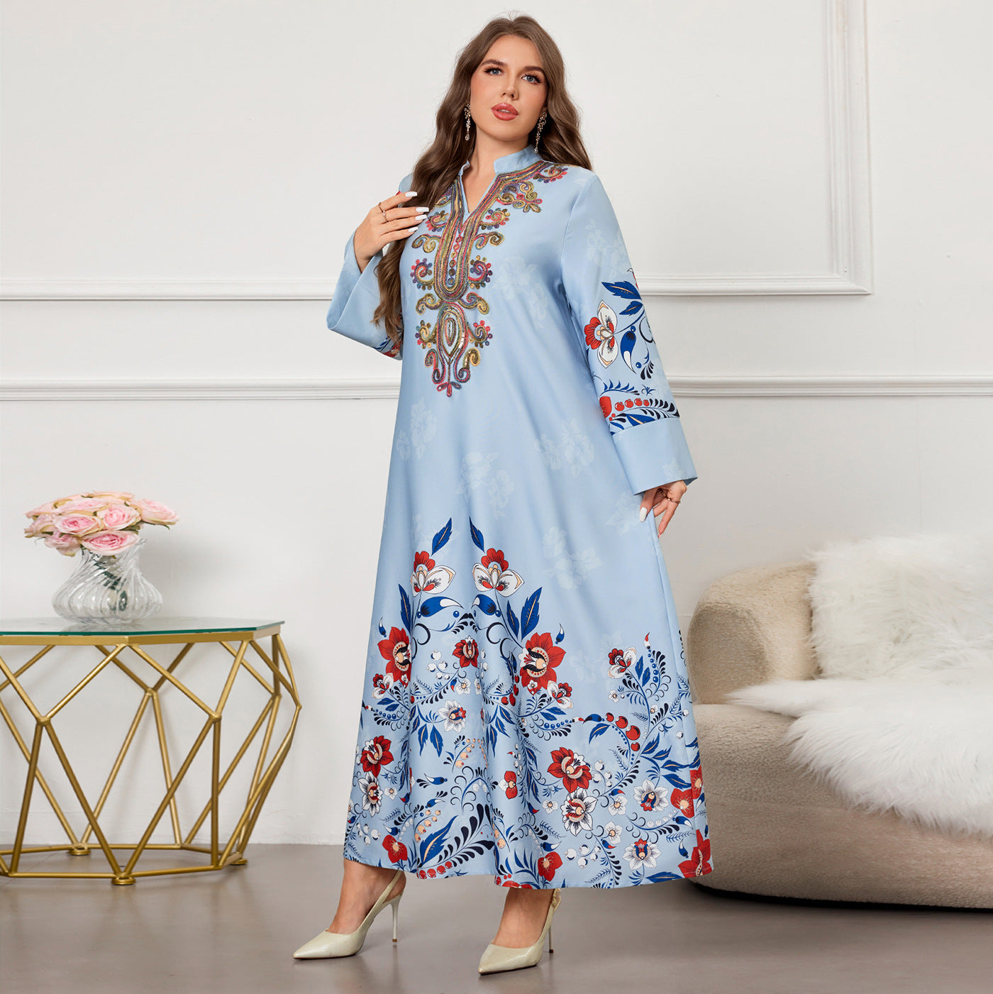 Woman wearing a light blue dress with floral embroidery in a room with a white wall and decorative elements.