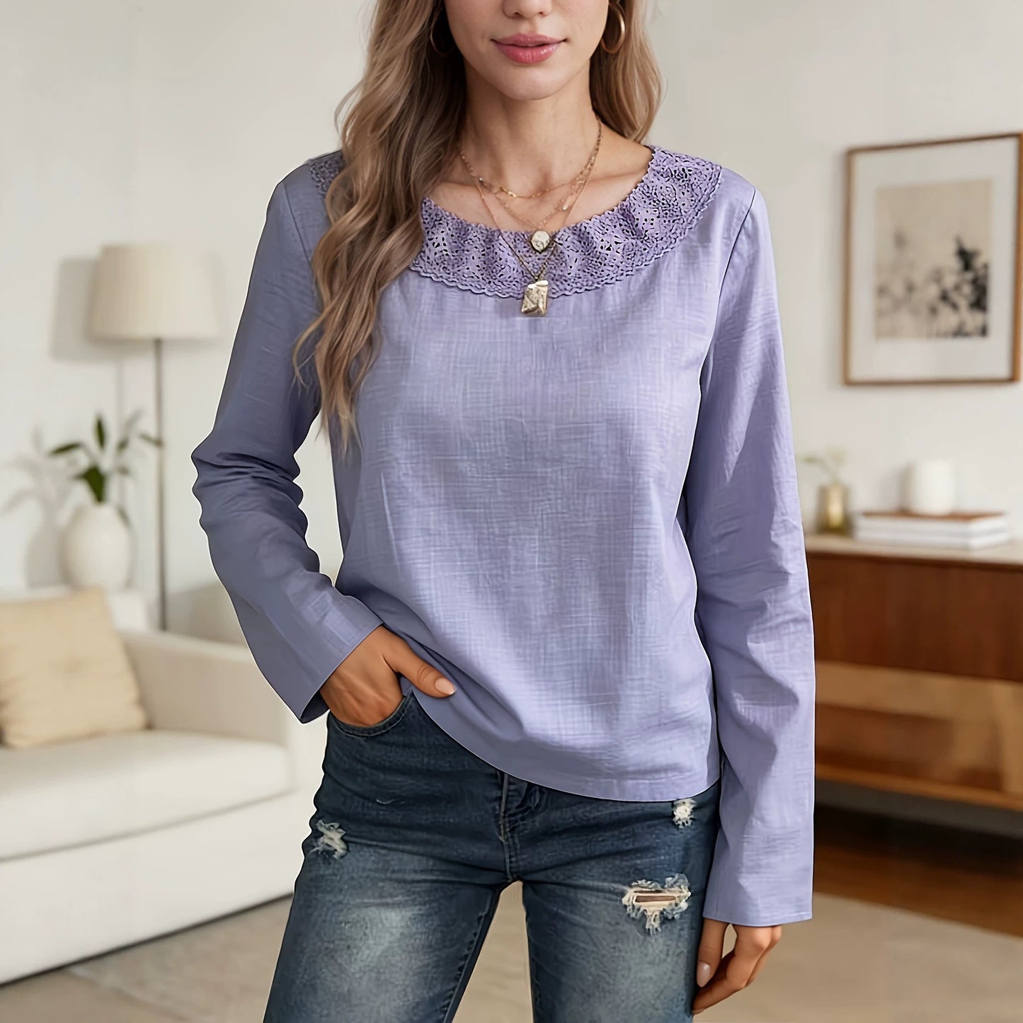 A woman wearing a lavender long-sleeve blouse with a lace-trimmed round neckline, paired with distressed blue jeans, standing in a bright, modern living room.