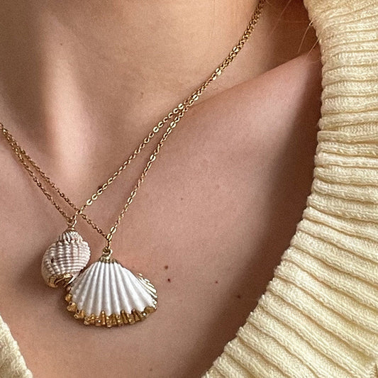 Gold necklace with shell pendants on a person wearing a beige top.