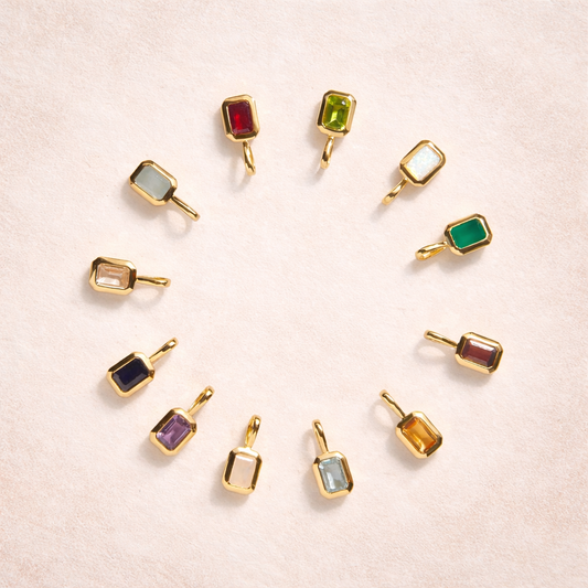 Gold charms with colorful gemstones arranged in a circular pattern on a light pink background