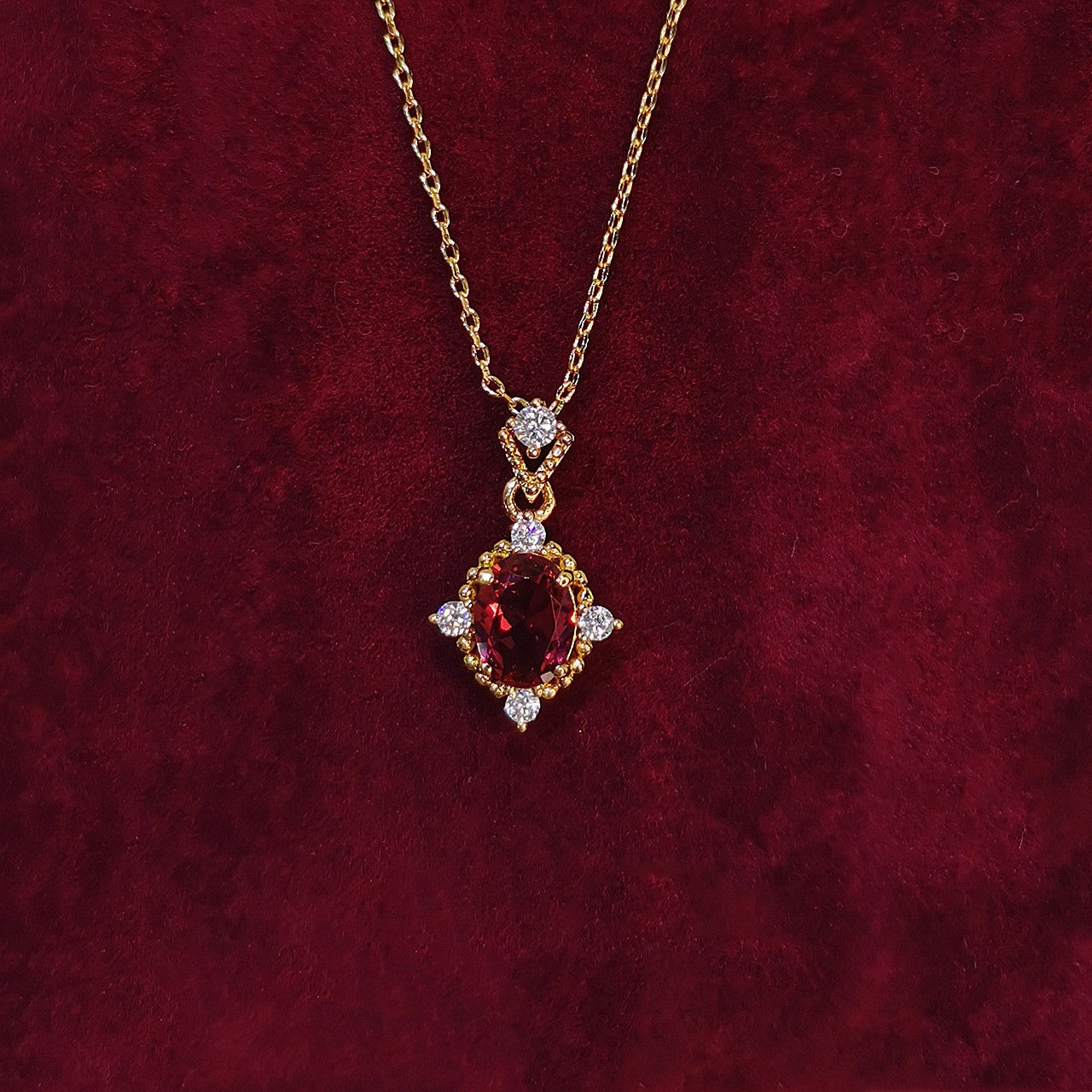 Gold necklace with a red gemstone pendant on a red velvet background